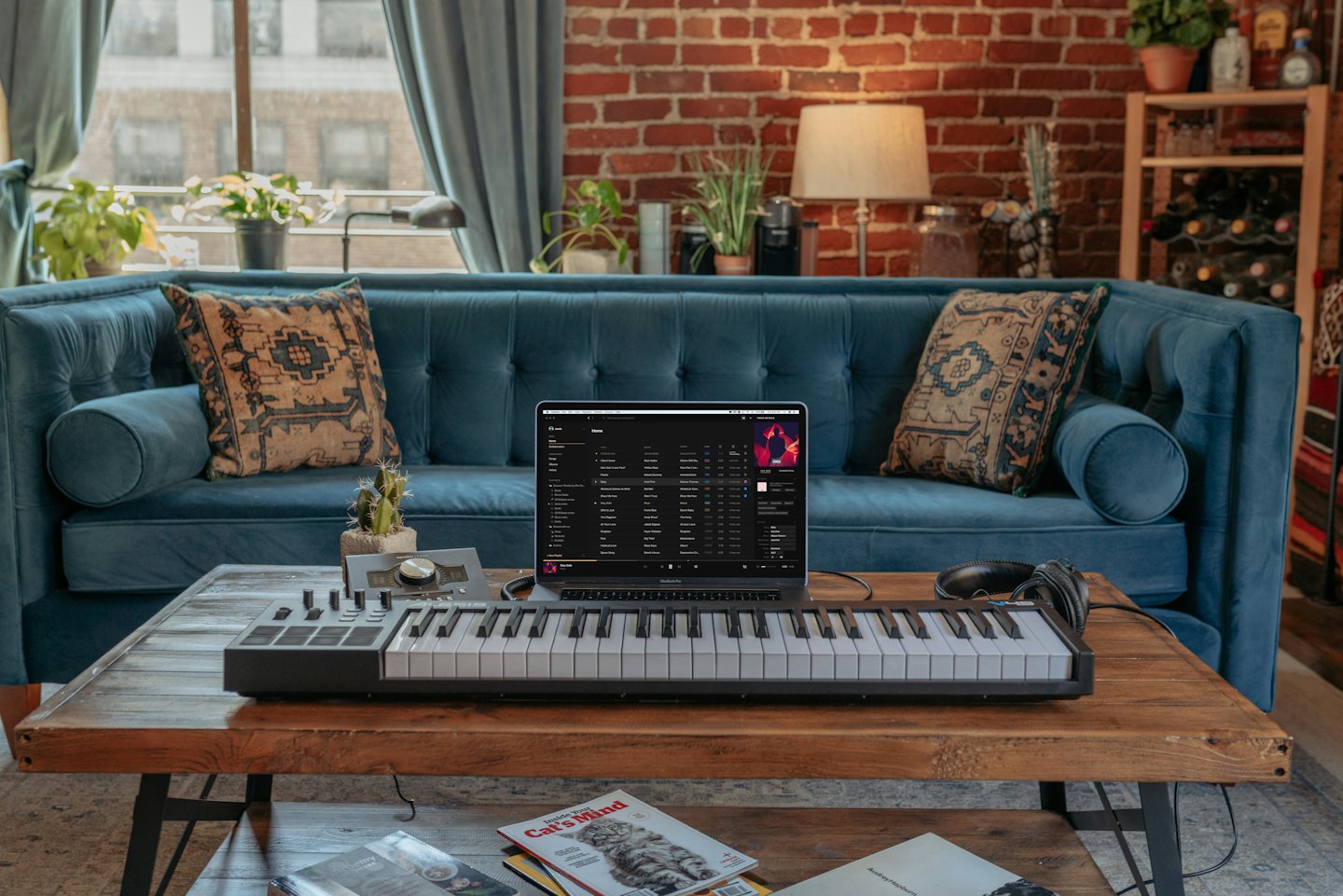 Laptop and MIDI keyboard on coffee table, with sofa and brick wall.