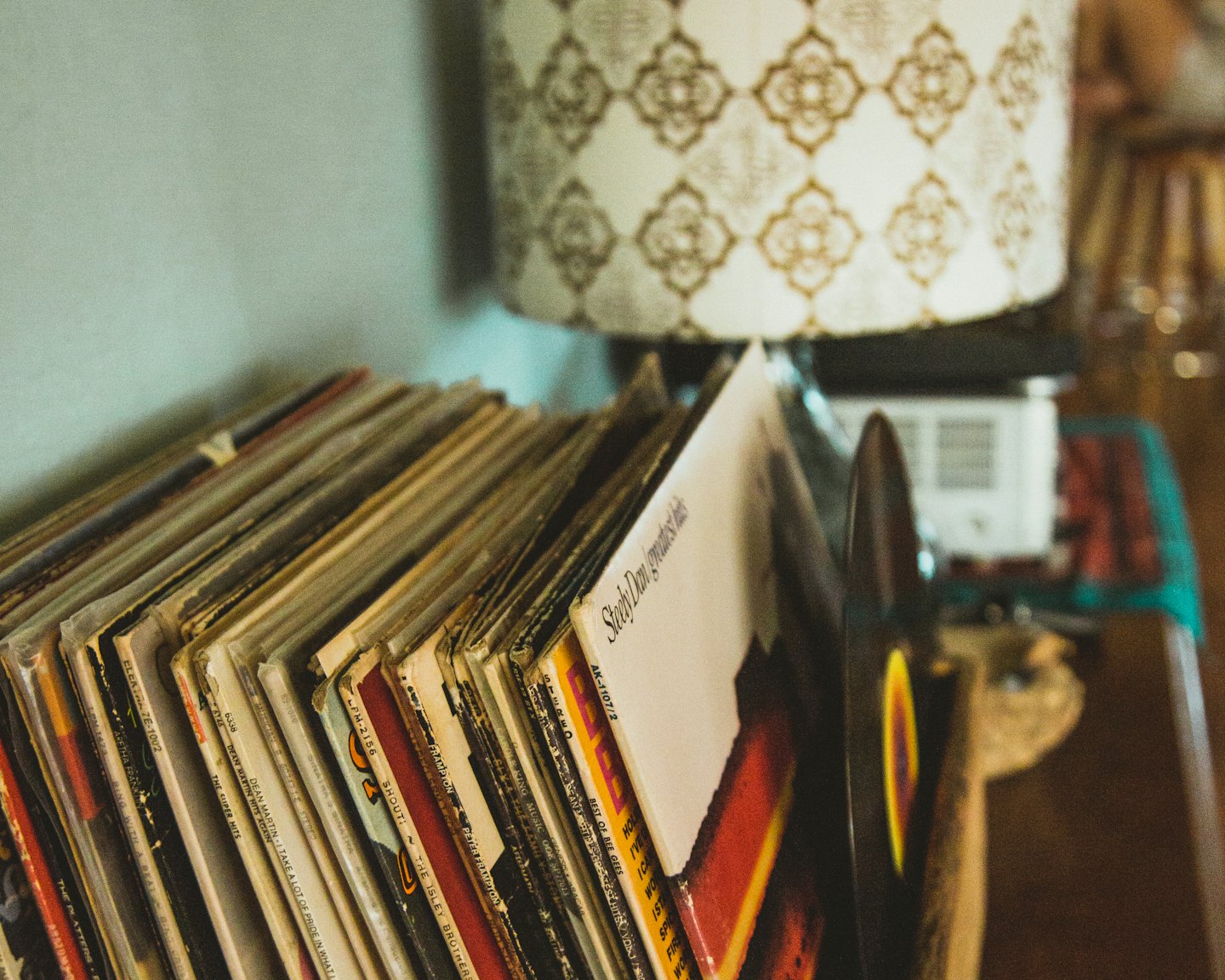 Stack of vintage vinyl records indoors next to a lamp.